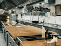 This image provides a view of a professional, commercial kitchen, focusing on a central wooden work surface in the foreground.