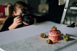 A photographer capturing the image of colorful donuts decorated with strawberries and sprinkles on a marble table