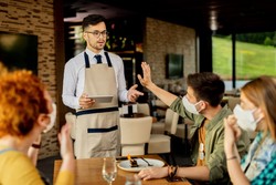 Manager with glasses and apron training the restaurant team about food waste.