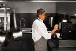 
This photograph shows a female chef operating a beverage machine in a professional kitchen.