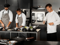 The image depicts a scene of teamwork and preparation inside a modern, professional kitchen.