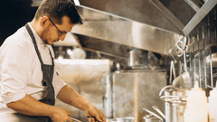 This image provides a close-up, profile view of a professional chef working intensely in a high-pressure kitchen environment.