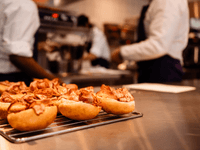 The image shows freshly prepared sandwiches with slices of cooked meat placed on a cooling rack in a professional kitchen.