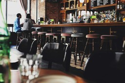 Image of a modern and cozy bar, showing people chatting and a variety of drinks. The atmosphere features a rustic and welcoming style.