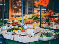This image captures a colorful and well-stocked outdoor market stall filled with fresh fruits and vegetables. Crates display vibrant produce like zucchinis, bell peppers, tomatoes, leafy greens, and mushrooms, each labeled with handwritten price tags. The setup is warm, inviting, and authentic — perfect for communicating freshness and local sourcing.
