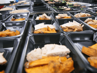  Rows of prepared meals in black containers inside a high-volume kitchen rental for large-scale food production.