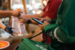 Delivery driver using a smartphone while picking up an order from a restaurant counter.