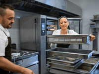 This photo shows a man and a woman working together in a professional kitchen. They both appear to be chefs or kitchen staff.