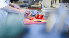 The image shows a chef working in a professional kitchen, preparing ingredients on a cutting board.