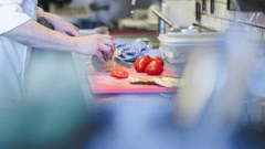 The image shows a chef working in a professional kitchen, preparing ingredients on a cutting board.