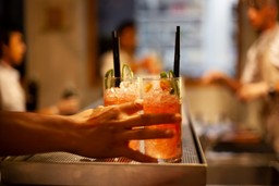 Two refreshing cocktails in tall glasses with ice, lemon, and straws, served at a bar. Perfect for those seeking flavorful drinks.