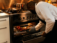The image shows a chef, who appears to be a Black man, wearing a white chef's jacket and a black apron.