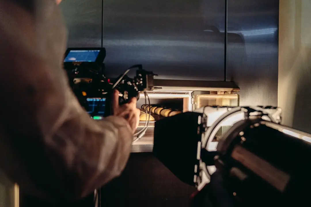 This is a photograph taken behind the scenes of a food production or commercial shoot, likely in a professional kitchen environment. The image is focused on the intense process of filming food.