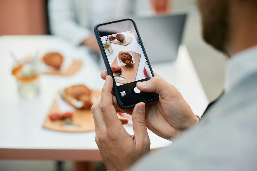 Man taking a food photo with smartphone for TikTok marketing for restaurants at a modern café table.